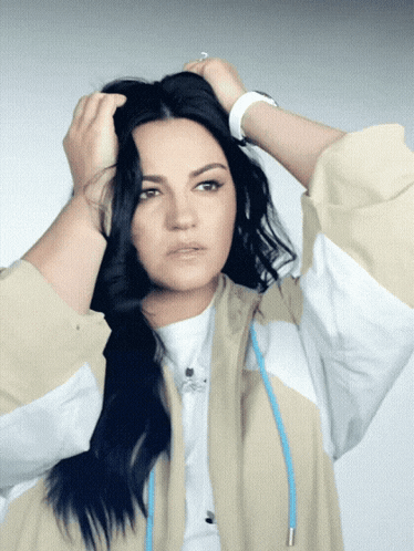 a woman in a tan and white jacket holds her hair up