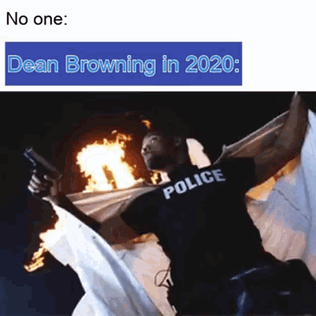 a man wearing a police shirt is holding a gun in front of a fire .