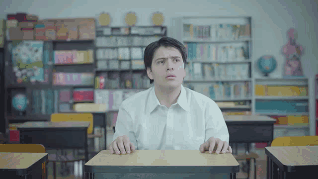 a man in a white shirt sits at a desk in a classroom looking up