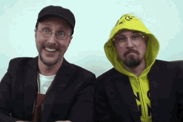 a man wearing a yellow hoodie with the letter g on it stands next to another man wearing glasses