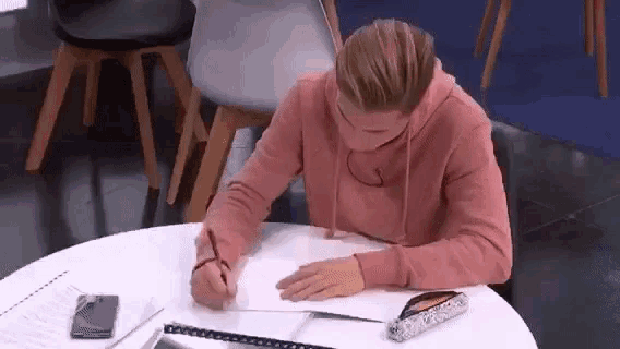 a young man is sitting at a table writing in a notebook .