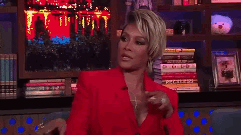 a woman in a red jacket is sitting in front of a bookshelf with books .