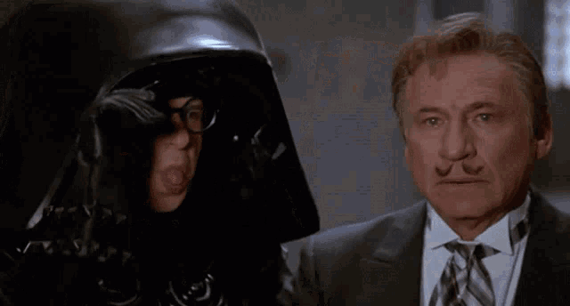 a man in a suit and tie is standing next to a man wearing a helmet