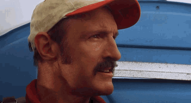 a man with a mustache wears a baseball cap and a red shirt
