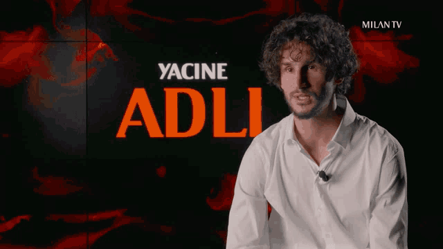a man in a white shirt is sitting in front of a wall that says milan tv