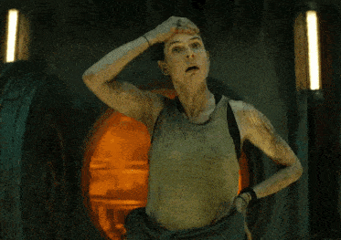 a woman in a tank top is standing in a dark room with her hand on her head