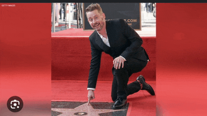 a man in a suit is kneeling down on a red carpet and pointing at a star