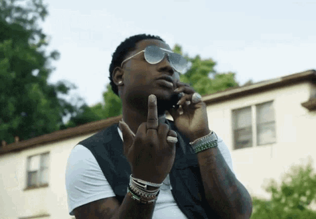 a man wearing sunglasses giving the middle finger while talking on a cell phone