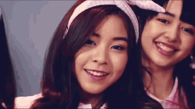 two young women are posing for a picture together and smiling . one of the girls is wearing a headband .