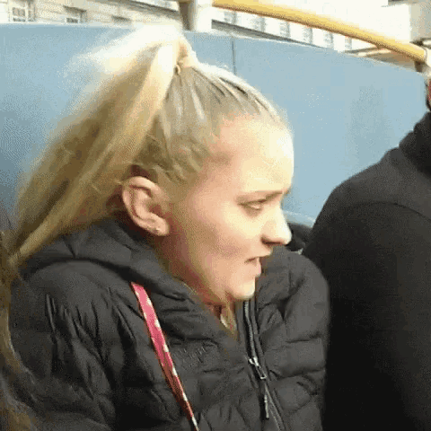 a woman with blonde hair is wearing a black jacket and has a ponytail .