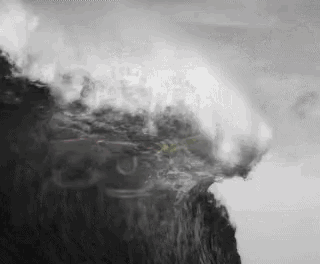 a black and white photo of a wave crashing against a cliff