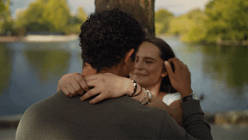 a man and a woman are hugging each other in front of a lake