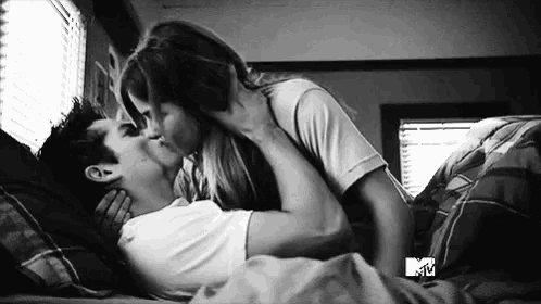 a black and white photo of a man and woman kissing on a bed .