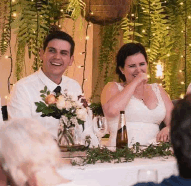 a bride and groom are sitting at a table laughing .