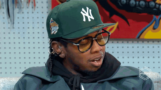 a man wearing a green ny hat and glasses is sitting on a couch