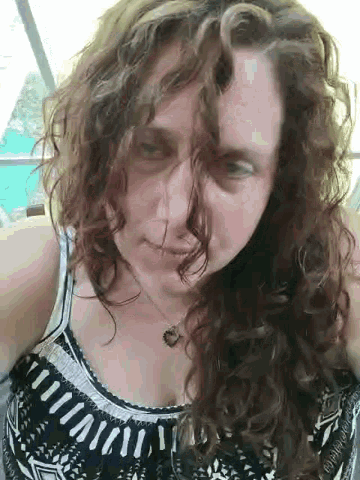 a woman with curly hair is wearing a black and white tank top and necklace .