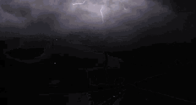 lightning strikes over a dark road with a street light in the foreground