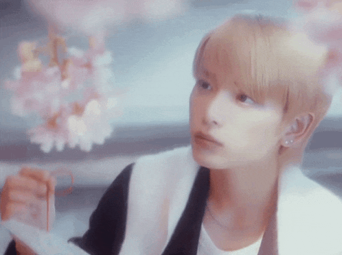 a young man with blonde hair is holding a bouquet of pink flowers in his hands .
