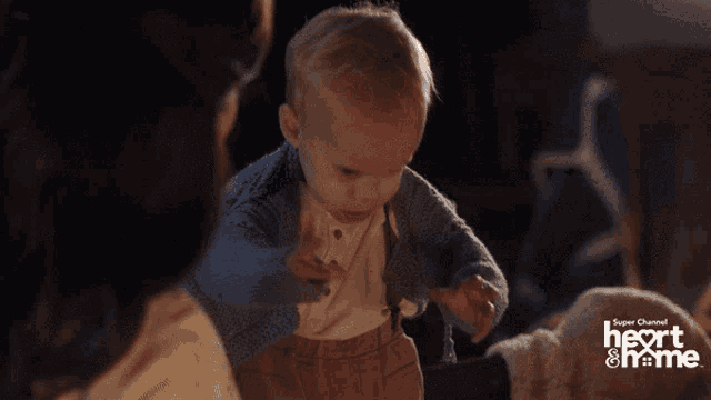 a baby in a blue sweater is being held by a woman in a super channel heart & home ad