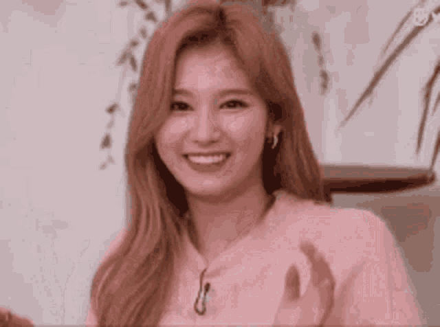a close up of a woman in a pink sweater clapping her hands and smiling .