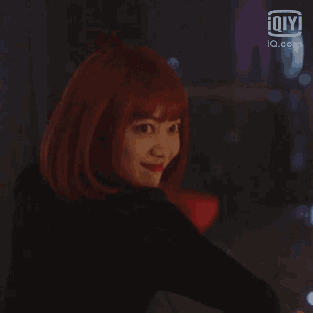 a woman with red hair and red lipstick is sitting at a table in a dark room