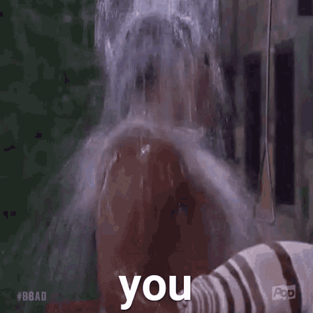 a man is taking a shower with water pouring on his head and says `` you '' .