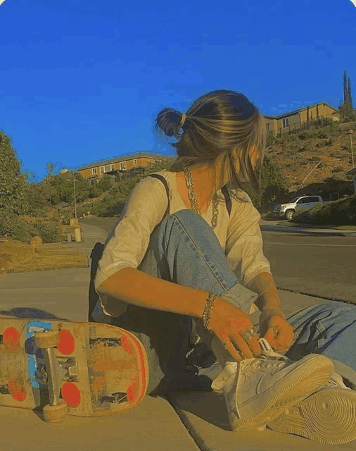 a girl sits on the sidewalk next to a skateboard that says sb on the front