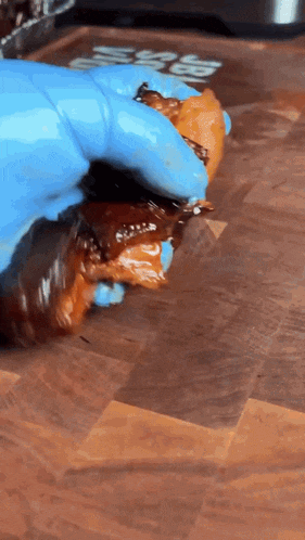 a person wearing blue gloves holds a piece of meat on a wooden cutting board