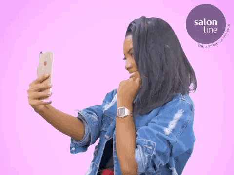 a woman in a denim jacket takes a selfie with a salon line logo in the background