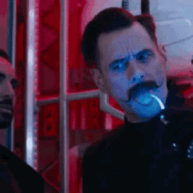 a man with a mustache is smoking a cigarette in a red room .