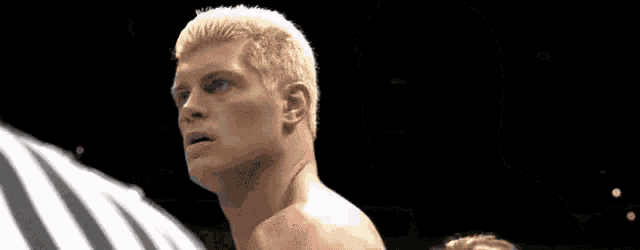 a man with blonde hair is standing in a boxing ring with a referee .