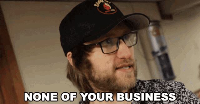 a man wearing glasses and a hat with the words none of your business below him