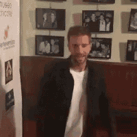 a man in a black jacket and white shirt is standing in front of a wall of pictures .