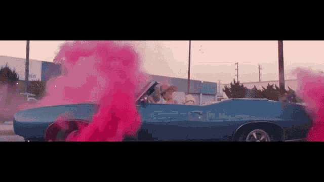 a woman is driving a blue car with pink smoke coming out of the car .