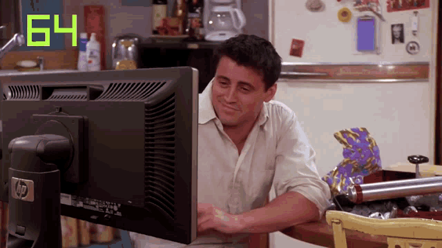 a man sits at a table looking at a computer monitor with the number 64 on it