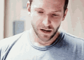 a man with a beard is wearing a blue t-shirt and looking down .