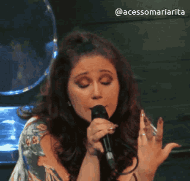 a woman singing into a microphone with the hashtag @acessomariarita on the bottom