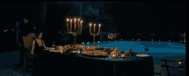 a woman sits at a table in front of a pool with candles on it
