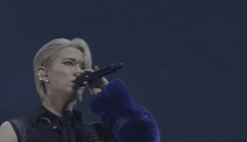 a man wearing a blue fur coat is singing into a microphone .
