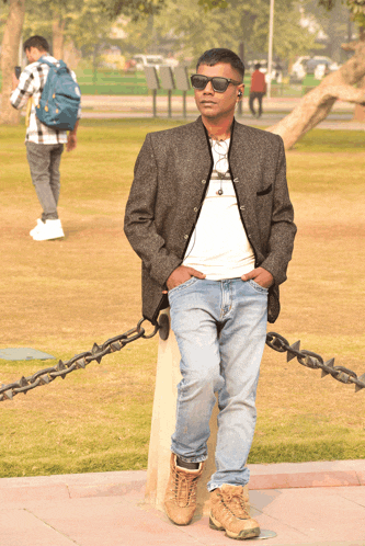a man wearing sunglasses is leaning against a chain link fence in a park