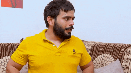 a man with a beard is sitting on a couch in a yellow shirt