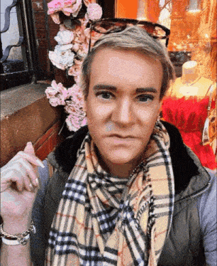 a man wearing a plaid scarf and sunglasses is standing in front of flowers