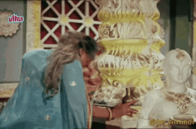 a woman in a blue dress is kneeling down in front of a statue with ultra written on the bottom