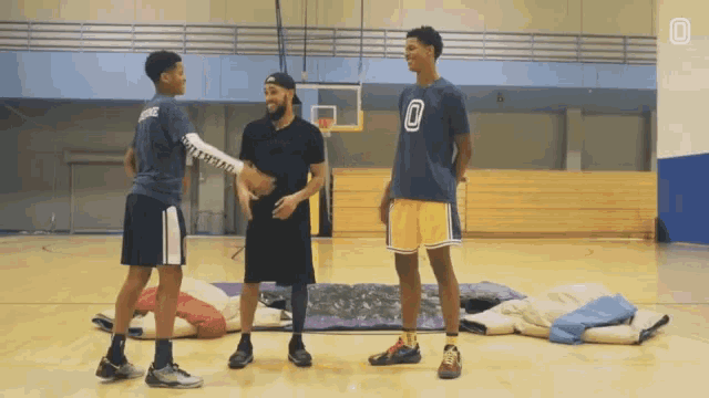a man wearing a number 0 shirt talks to two other men on a basketball court