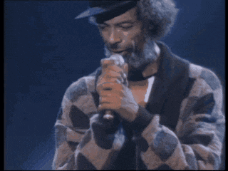 a man singing into a microphone with a hat on