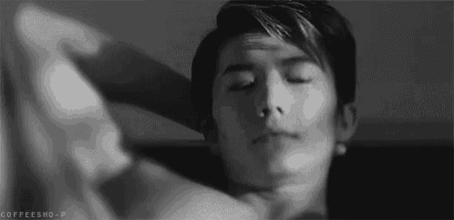 a black and white photo of a man with his eyes closed and his hand on his head .