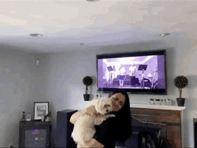 a woman is holding a small dog in her arms in a living room while watching a tv .