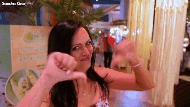 a woman giving a thumbs down sign in front of a sign that says sandra cire3art