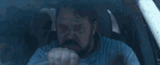 a man with a beard is driving a car and making a face .