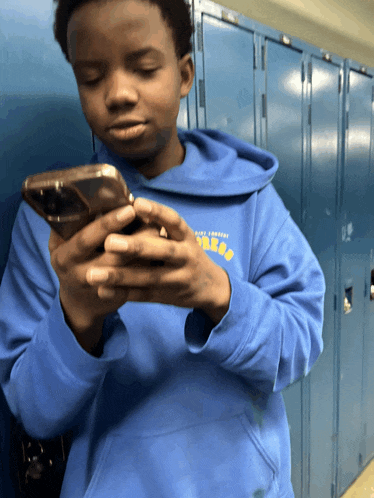 a boy wearing a blue sweatshirt that says ucla looks at his phone